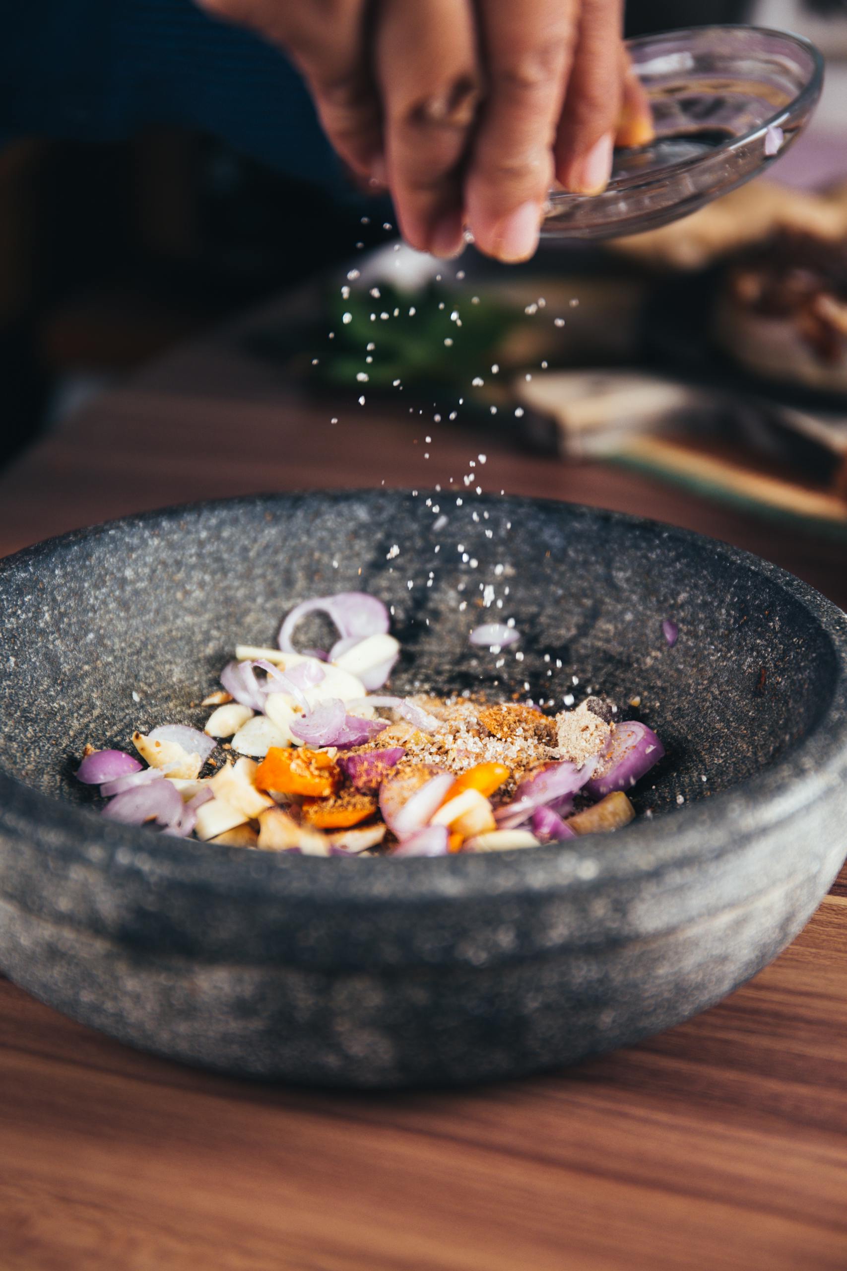 Close-up of seasoning being added to fresh ingredients in a stone bowl, perfect for culinary themes.